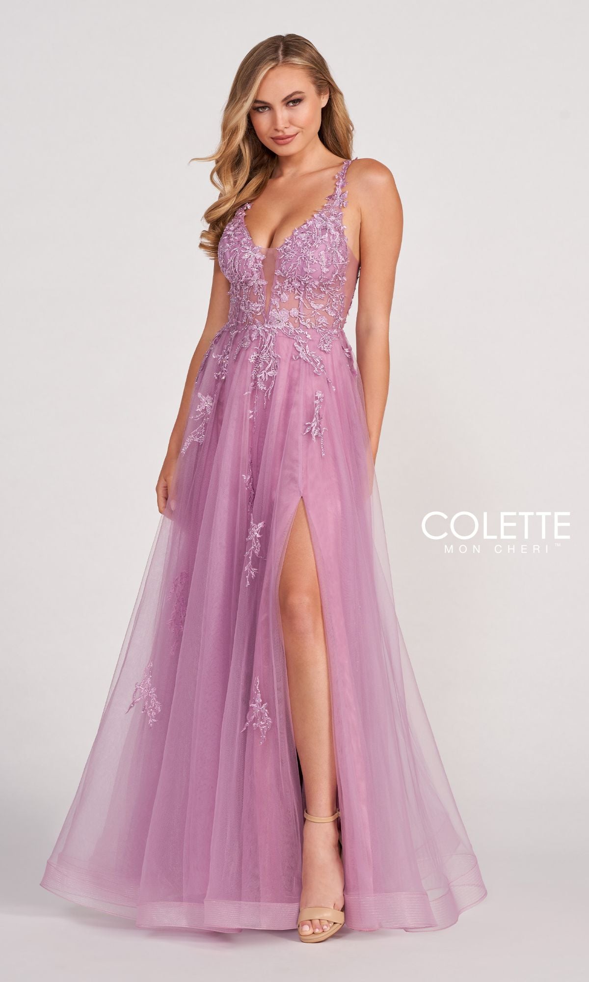A woman wears the CL2074 Tulle A-Line Prom Dress with a sheer bodice, sleeveless design, floor-length mauve tulle, lace appliques, floral embellishments, a deep V-neckline, and high slit by Colette Mon Cheri.